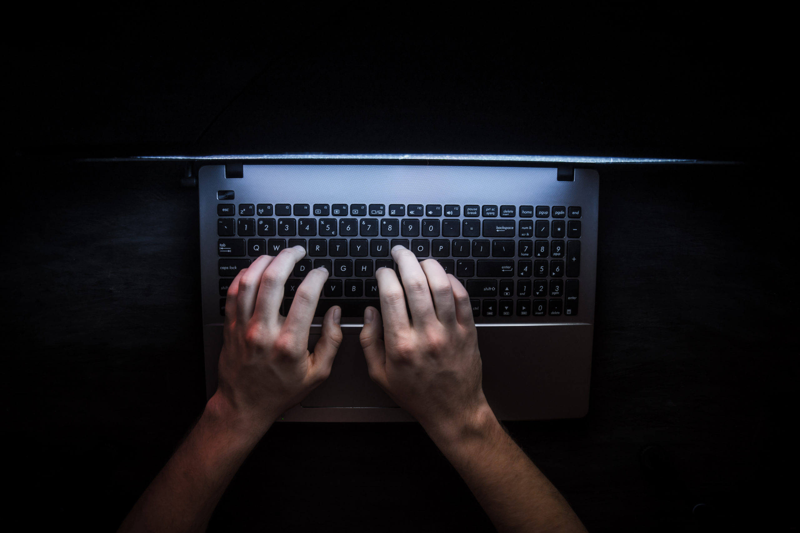  Hacker in dark room on laptop attempting a data breach.