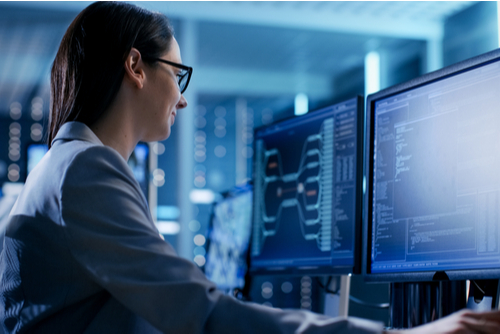 Female cybersecurity professional works in control room with dual monitors. 