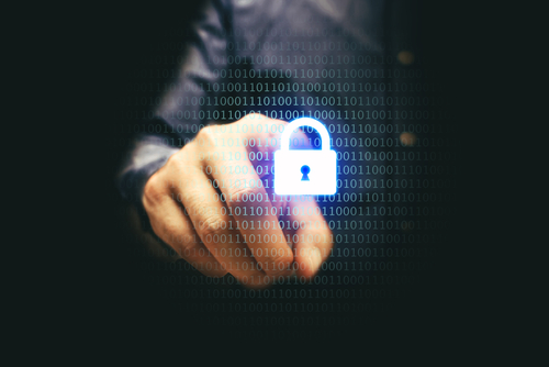 A man’s finger touches a brightly-lit padlock graphic that is illuminating a dark room. 