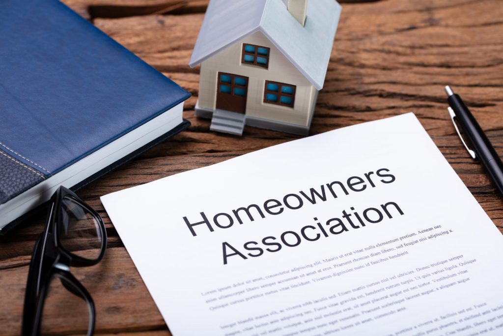 Close up of a homeowners association contract lying on a desk with a pen and small figurine of a house. 