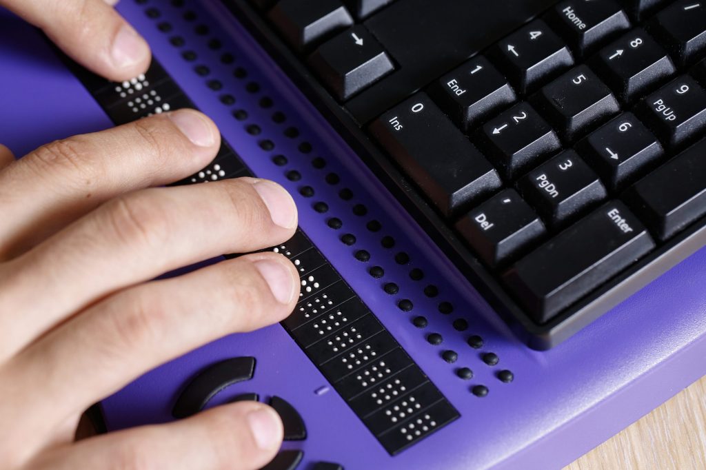 Close up of a blind person’s hands utilizing computer keyboard braille.