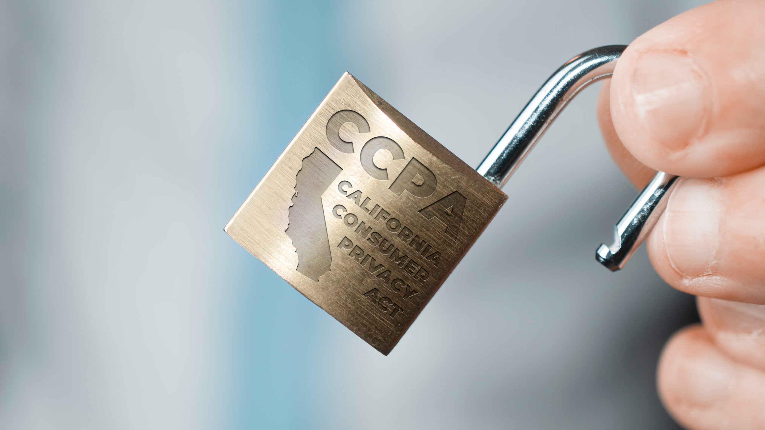 Close up of hand holding open brass padlock engraved with shape of California and text “CCPA California Consumer Privacy Act.”