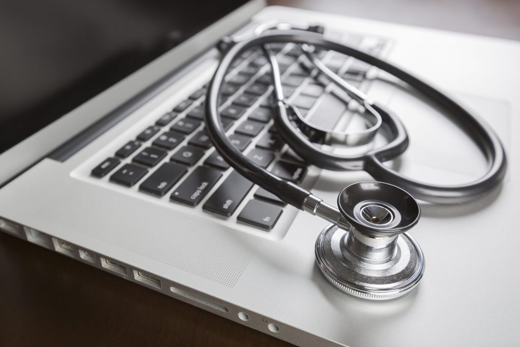 A stethoscope lays on the keyboard of a silver laptop. 