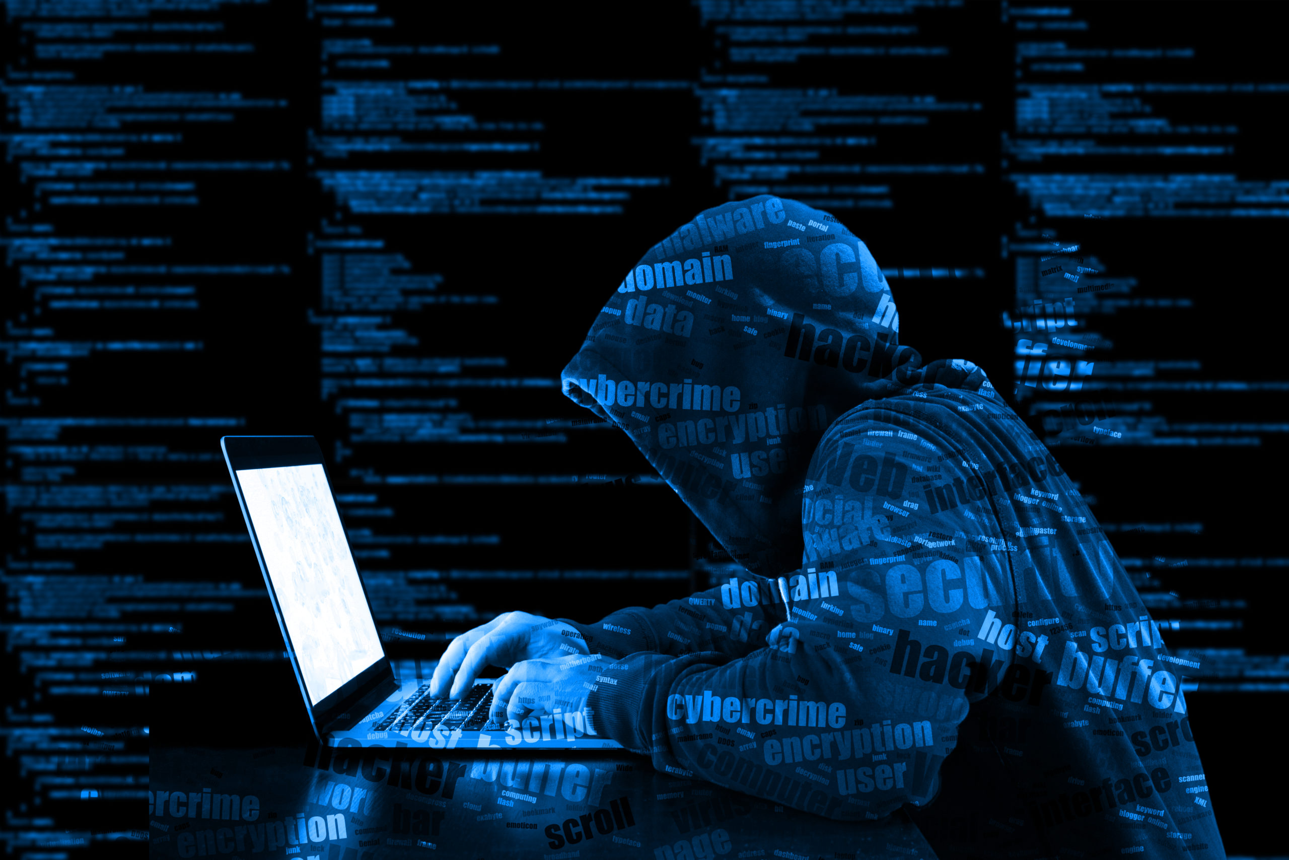 Hacker in hoodie types on laptop computer, code streaming in background, illustrating need for cyber risk liability insurance.