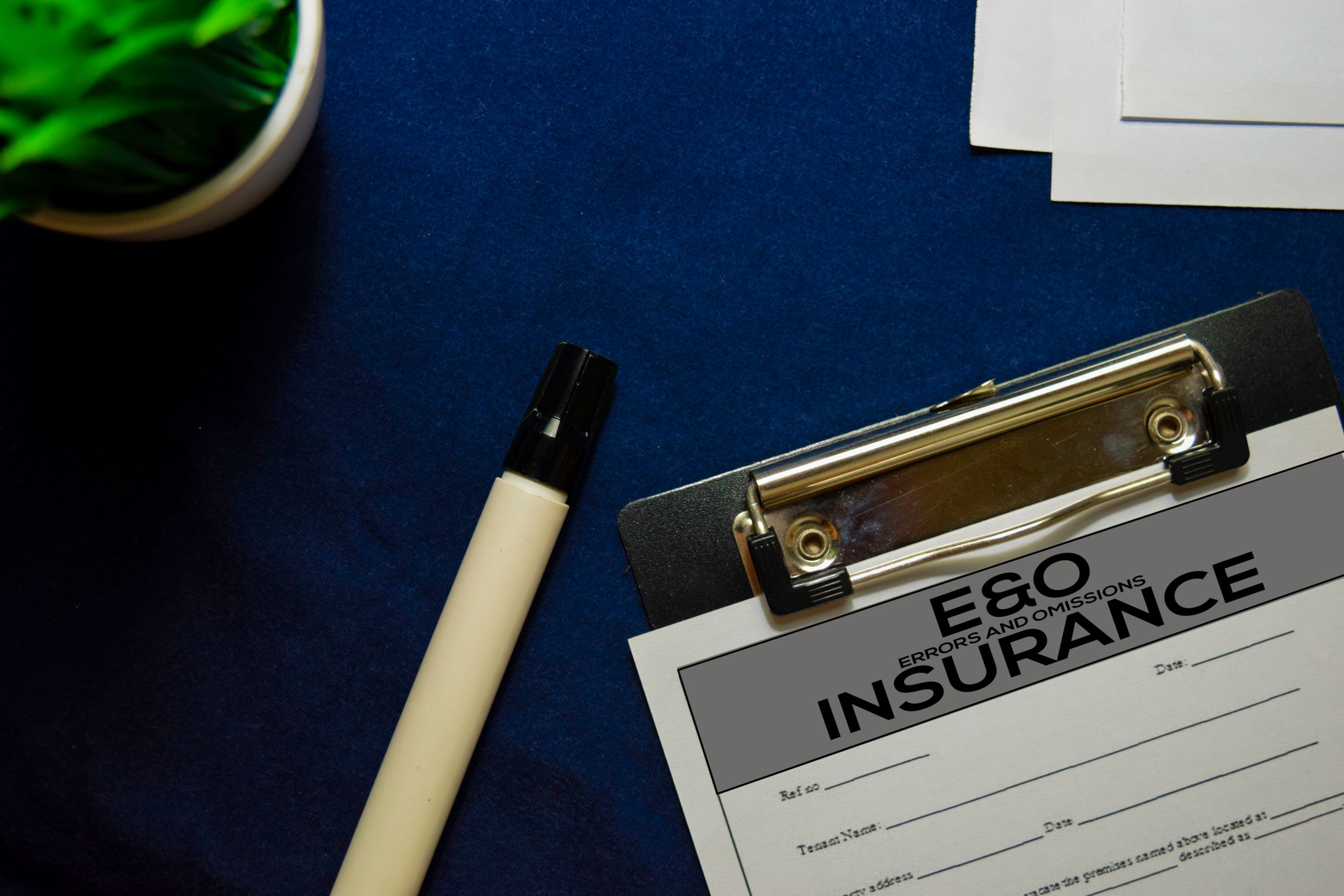 Capped marker lies next to clipboard on desktop, paper form on clipboard is titled “E&O Insurance.”