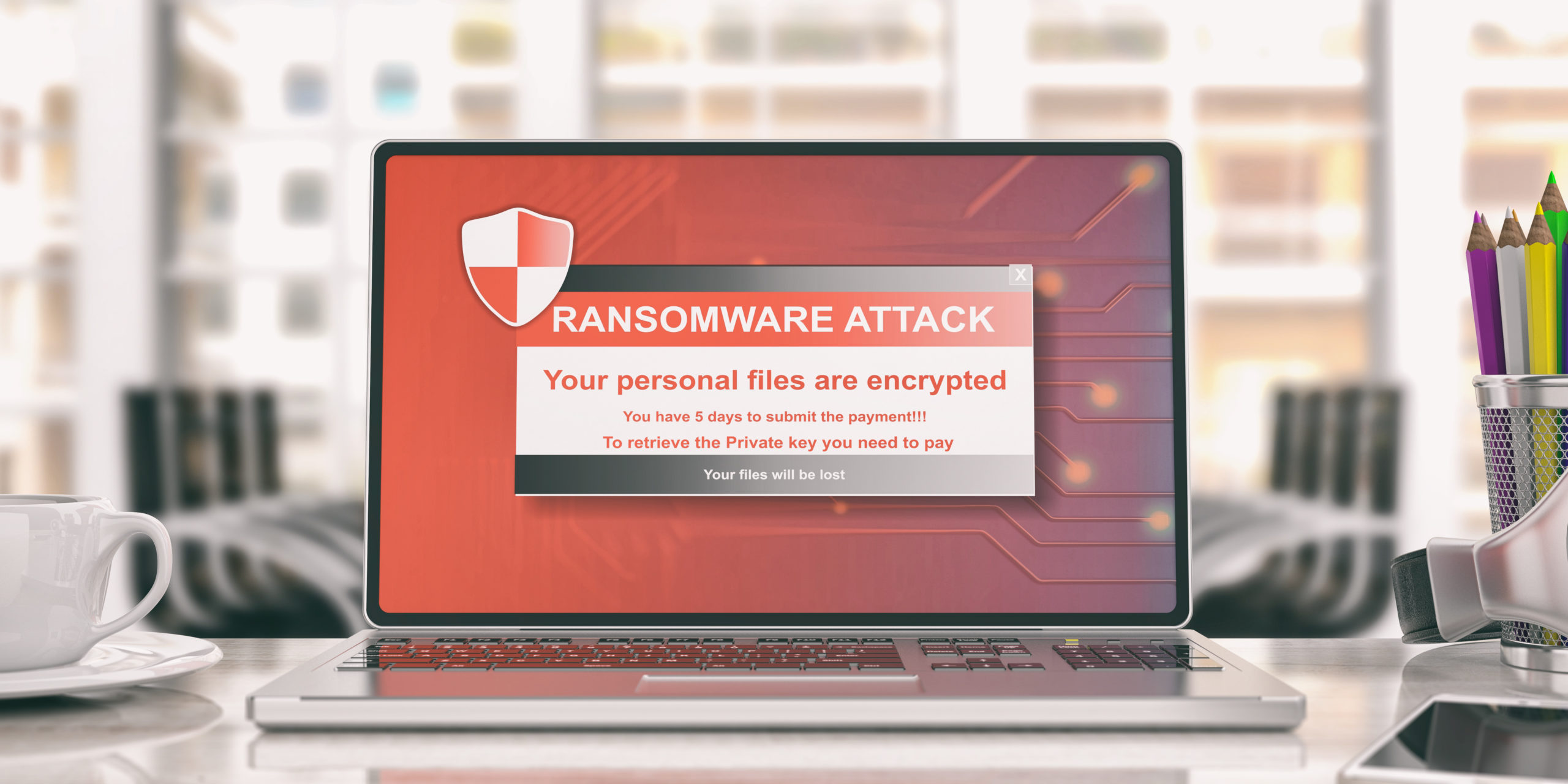  Computer laptop sits on office desk, its screen with warning reading, “RANSOMWARE ATTACK. Your personal files are encrypted.”