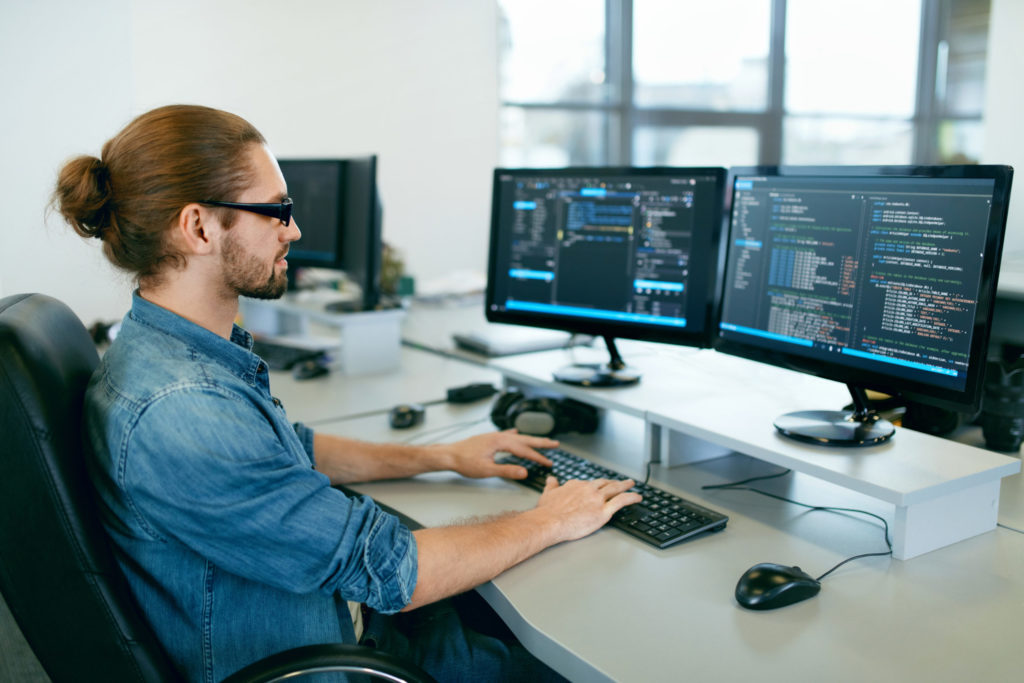Man with two monitors looks at code. 