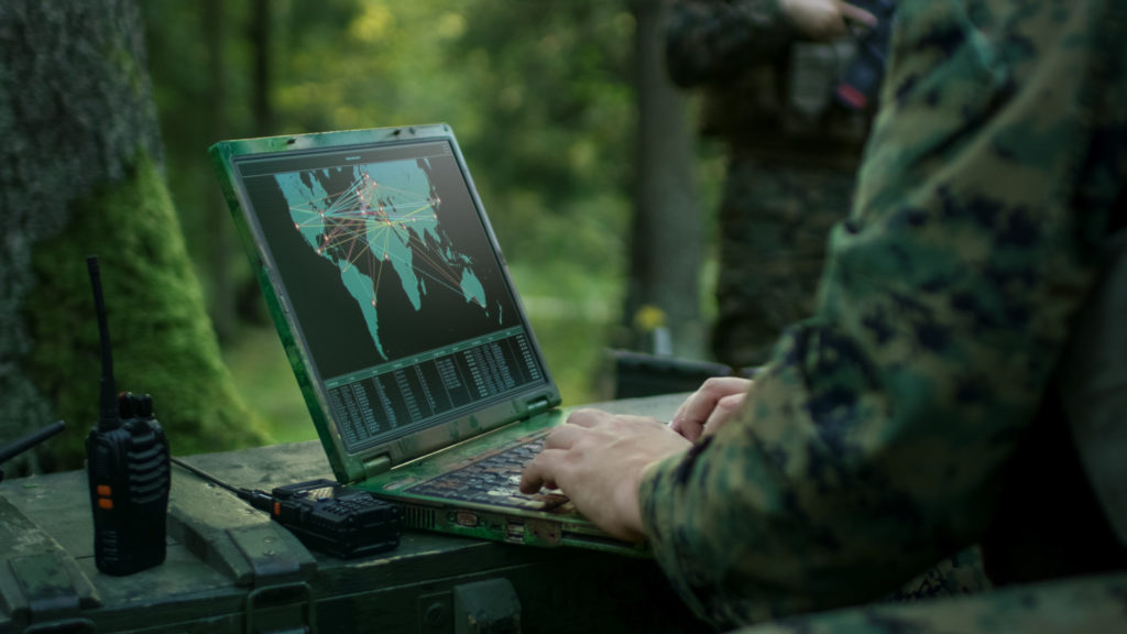 Soldier in the woods on his laptop as he hacks into enemy systems. 