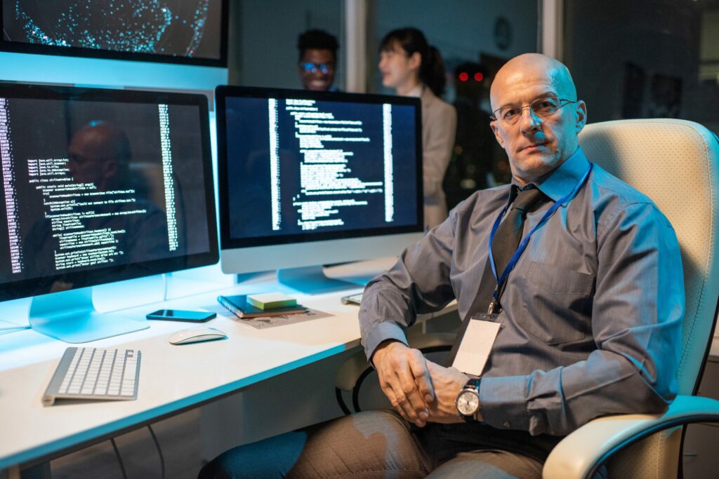  IT forensic engineer sits at his workstation with two large monitors, representing an MDR service, a key cyber security control.