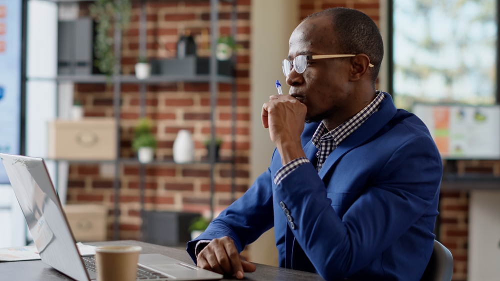 Cyber insurance broker sits at his desk with a laptop computer, reviewing cyber liability options for his business clients.