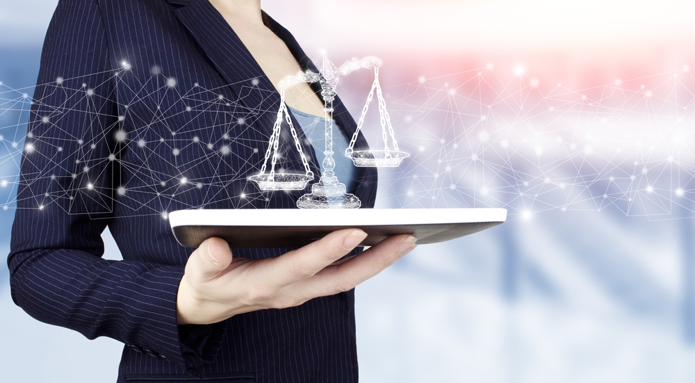 Lawyer holds tablet computer, digital image of scales of justice superimposed, suggesting data security litigation. 