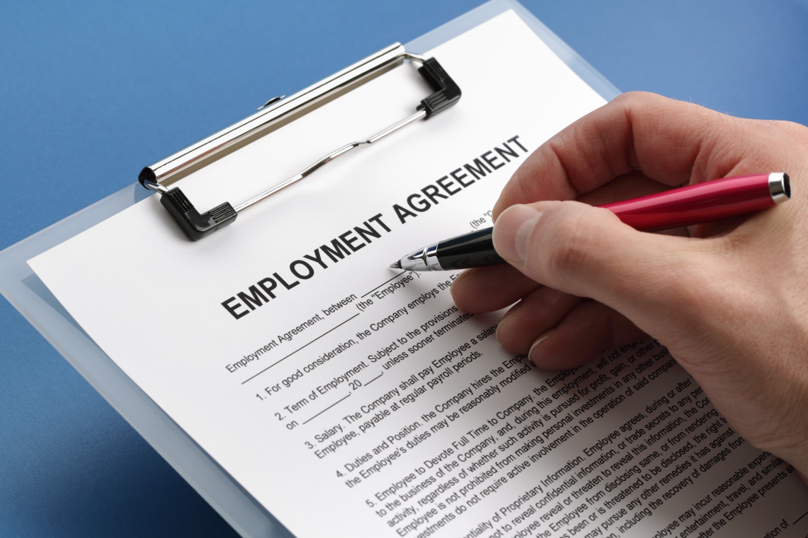 Hand using ballpoint pen to sign an employment contract.
